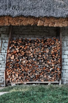 Logs of firewood stored under the stone shed. Stacked firewood in a backyard back of house