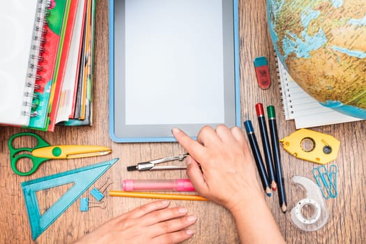 Female hand using tablet. School accessories, pencil, pen, scissors and tablet with blank screen on a wooden desk