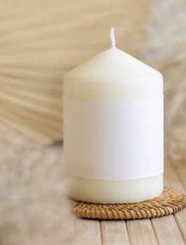 Candle with blank paper label on wooden table with dried pampas grass, Close up, copy space. Minimal brand packaging mock up. Home decoration, minimal interior, Bohemian or scandinavian style