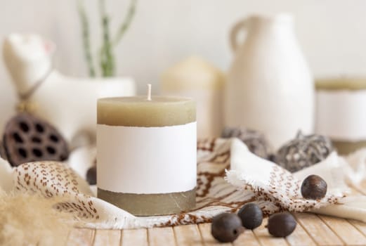 Candle with blank paper label on wooden table near natural decor Close up, copy space. Boho or ethnic packaging mock up. Home decorations in Bohemian or scandinavian style