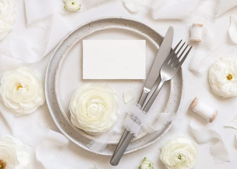 Wedding table setting with card near cream roses and white silk ribbons top view, mockup. Romantic scene with horizontal table place card and pastel flowers. Valentines, Spring or Mothers day concept