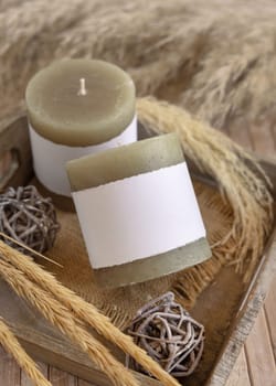Candle with blank paper label on wooden tray near dried pampas grass and natural decor, Close up, copy space. Boho packaging mock up. Home decorations, Bohemian or scandinavian style
