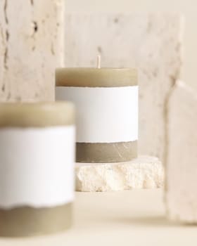 Candles with label on beige near cream travertine stones, Close up, copy space. Brand packaging mock up. Home decoration, minimal interior, Bohemian or scandinavian style