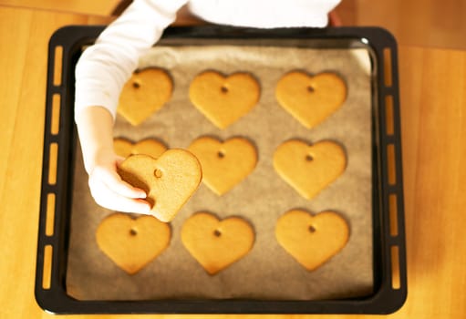 A girl hand holding a heart cookie in front of the homemade fresh baked cookies on baking sheet.