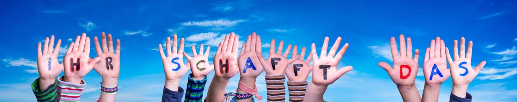 Children Hands Building Colorful German Word Ihr Schafft Das Means You Can Do It. Blue Sky As Background.