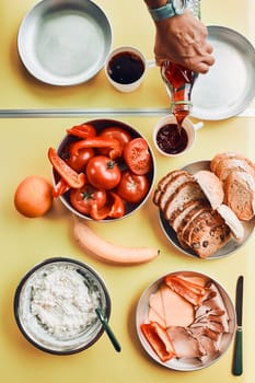 Breakfast prepared during summer vacation on camping. Bread, cottage cheese, cold meat, tomatoes, fruits and coffee cups on table. Close up of outdoor table setting from above