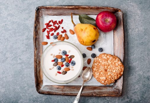 Breakfast on table. Yogurt with added blueberries and roasted almonds. Muesli cookie, apples and pears on table. Light and healthy meal. Good quality balanced diet. Flat top-down composition