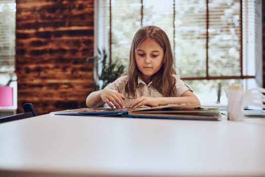 Girl learning, playing, doing puzzles and reading book in afterschool club. Primary school pupil is engaged in book with jigsaw. Smart girl learning from book. Benefits of everyday reading. Child curiosity