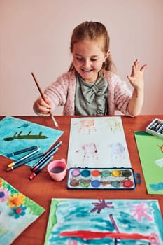 Little girl preschooler painting a picture using colorful paints and crayons. Child having fun making a picture during an art class in the classroom