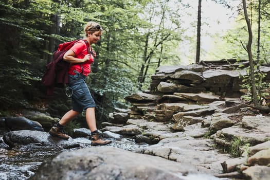 Woman with backpack hiking in mountains, spending summer vacation close to nature. Woman crossing the mountain stream