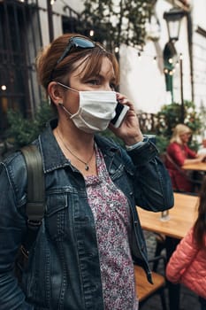 Young woman talking on phone standing in a street downtown. Woman is wearing the face mask to avoid virus infection and to prevent the spread of disease in time of coronavirus