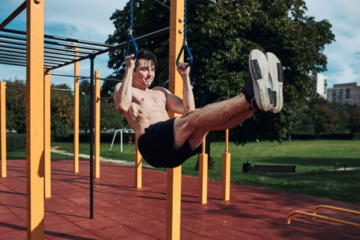 Young shirtless man bodybuilder doing L-Sit during his workout in a modern calisthenics street workout park