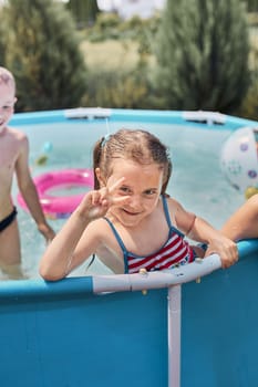 Happy girl making V sign gesture playing in a pool enjoying splashing having fun with siblings on a summer sunny day