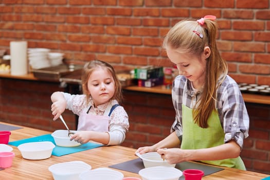 Little girls stirring the yolk with sugar. Kids taking part in baking workshop. Baking classes for children,  aspiring little chefs. Girls learning to cook. Combining and stirring prepared ingredients. Real people, authentic situations
