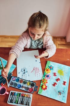 Little girl preschooler painting a picture using colorful paints and crayons. Child having fun making a picture during an art class in the classroom