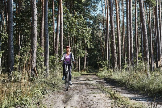 Active woman cycling on forest road. Female riding bicycle off-road route on summer vacation day. Woman wearing bicycle helmet and gloves