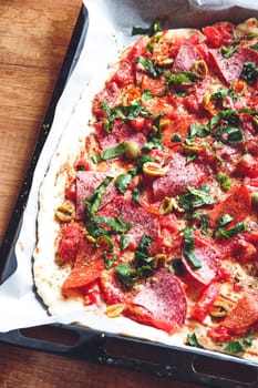 Pizza on tray topped with tomato, sauce, cheese, meat, vegetales, fruits and herbs