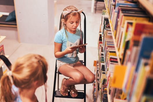 Schoolgirls looking for audio books in school library. Students choosing set books. Elementary education. Doing homework. Learning from books. Back to school