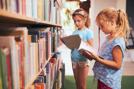 Two schoolgirls choosing books in school library. Primary school students learning from books. Children having fun in school club. Back to school. Doing homework