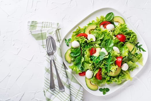 Fresh green salad with avocado, mozzarella cheese and tomato on white table background