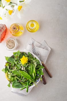 Healthy salad with spring plants and herbs. Dandelion, wild garlic, asparagus, flowers and nettle om bright table background