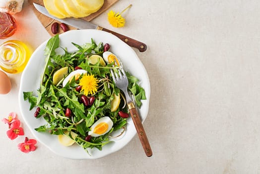 Dandelion salad with eggs, potato and beans on bright table background closeup
