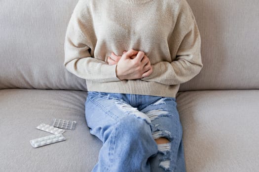 Young caucasian female experiencing stomach pain in casual attire on sofa.