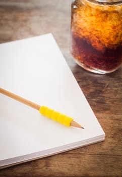 Pencil on open blank notebook with glass of iced cola, stock photo
