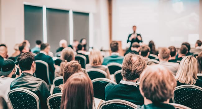 Speaker giving a talk in conference hall at business event. Rear view of unrecognizable people in audience at the conference hall. Business and entrepreneurship concept