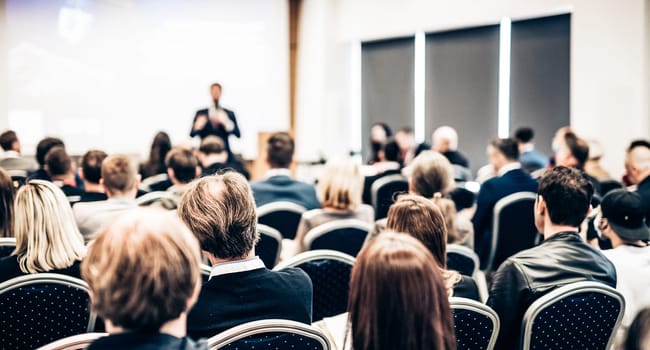 Speaker giving a talk in conference hall at business event. Rear view of unrecognizable people in audience at the conference hall. Business and entrepreneurship concept