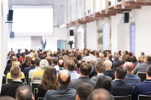 Speaker giving a talk in conference hall at business event. Audience at the conference hall. Business and Entrepreneurship concept. Focus on unrecognizable businessman in the audience.