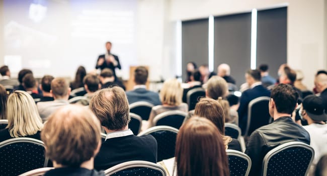 Speaker giving a talk in conference hall at business event. Rear view of unrecognizable people in audience at the conference hall. Business and entrepreneurship concept