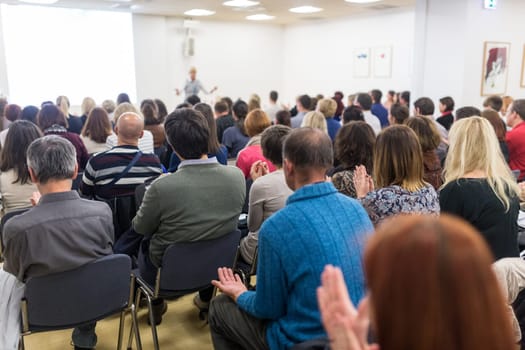 Life coaching symposium. Female speaker giving interactive motivational speech at entrepreneurship workshop. Audience in conference hall. Rear view of unrecognized participant.