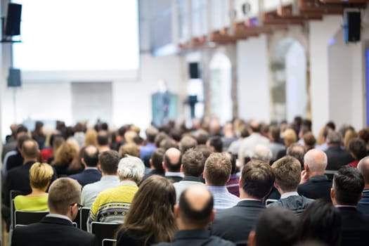 Speaker giving a talk in conference hall at business event. Audience at the conference hall. Business and Entrepreneurship concept. Focus on unrecognizable businessman in the audience.