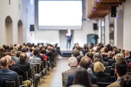 Speaker giving a talk in conference hall at business event. Audience at the conference hall. Business and Entrepreneurship concept. Focus on unrecognizable man in the audience.