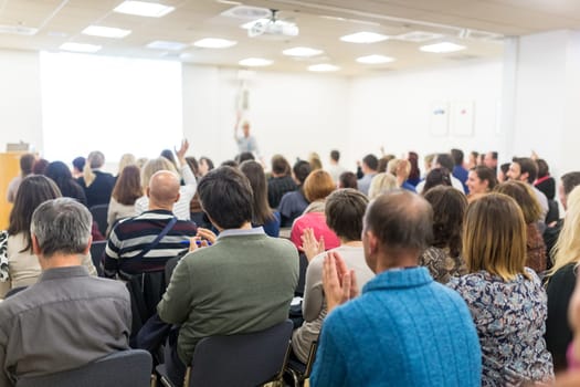 Life coaching symposium. Female speaker giving interactive motivational speech at entrepreneurship workshop. Audience in conference hall. Rear view of unrecognized participant.