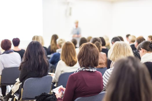 Business and entrepreneurship symposium. Female speaker giving a talk at business meeting. Audience in conference hall. Rear view of unrecognized participant in audience. Copy space on whitescreen.