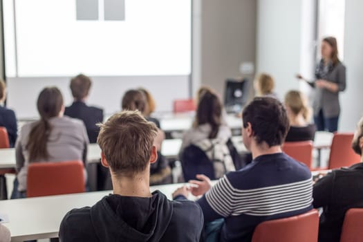Female speaker giving presentation in lecture hall at university workshop. Audience in conference hall. Rear view of unrecognized participant in audience. Scientific conference event.