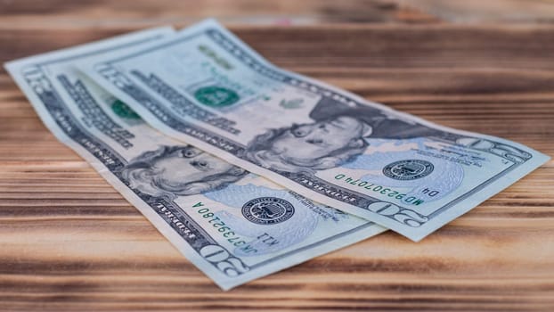 Two 20 US dollars bills, lying on a burnt wooden table top.