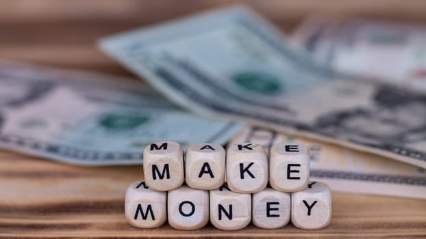 The words Make Money, lined with letters on wooden cubes on the background of dollar bills.
