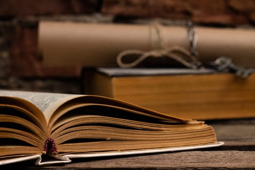 Old books with a scroll and key on a rustic wooden surface on a brick wall background