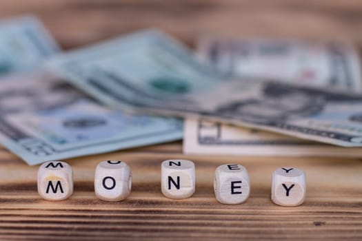The word Money, lined with letters on wooden cubes on a background of dollar bills.