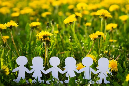 Silhouettes of children holding hands cut out of cardboard on a background of dandelions. Girls and boys made of white paper. International children's day. Copy space