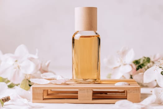 Cosmetic, aroma or massage oil on wooden podium in form of pallet on light plaster surface with apple flowers