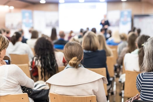 Speaker giving a talk in conference hall at business event. Audience at the conference hall. Business and Entrepreneurship concept. Focus on unrecognizable people in audience.