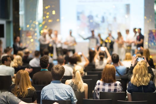 Young business team receiving award prize at best business project competition event. Business and entrepreneurship award ceremony theme. Focus on unrecognizable people in audience.