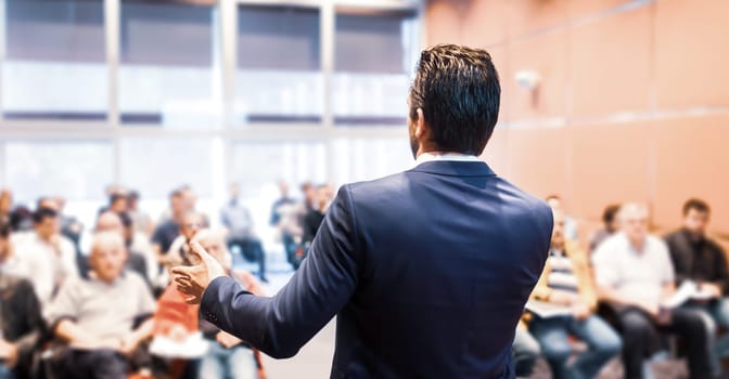 Speaker at Business Conference with Public Presentations. Audience at the conference hall. Entrepreneurship club. Rear view. Horisontal composition. Background blur.