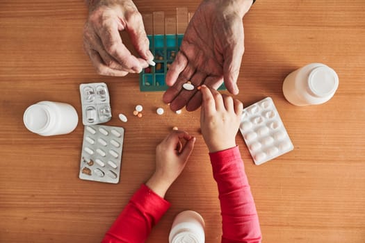 Grandchild helping grandfather to organize medication into pill dispenser. Senior man taking pills from box. Healthcare and old age concept with medicines. Medicaments on table