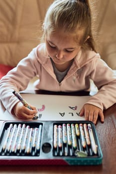 Little girl preschooler learning to write letters at home. Kid using crayons doing homework. Concept of early education