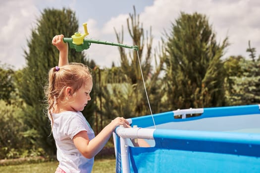 Children playing in a pool with fishing rod toy in a home garden. Kids having fun playing together on a summer sunny day